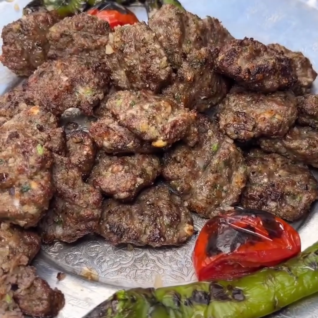 Browned kofte kebab patties on a silver platter with grilled red and green peppers